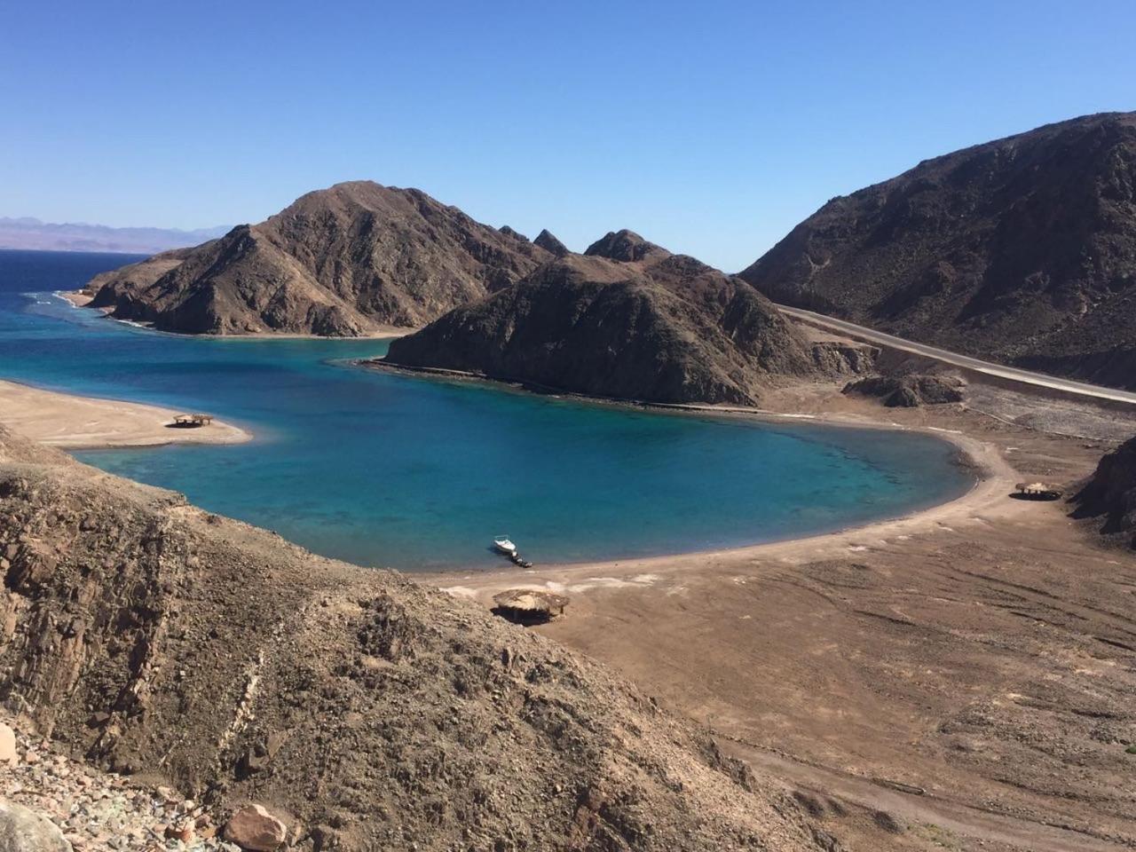 Steigenberger Hotel & Nelson Village, Taba Exterior foto The photo features a scenic landscape of rocky hills surrounding a calm blue body of water. The water appears to be in a bay or cove, with sandy shores visible on one side. In the background, there are more rugged mountains rising against a clear blu