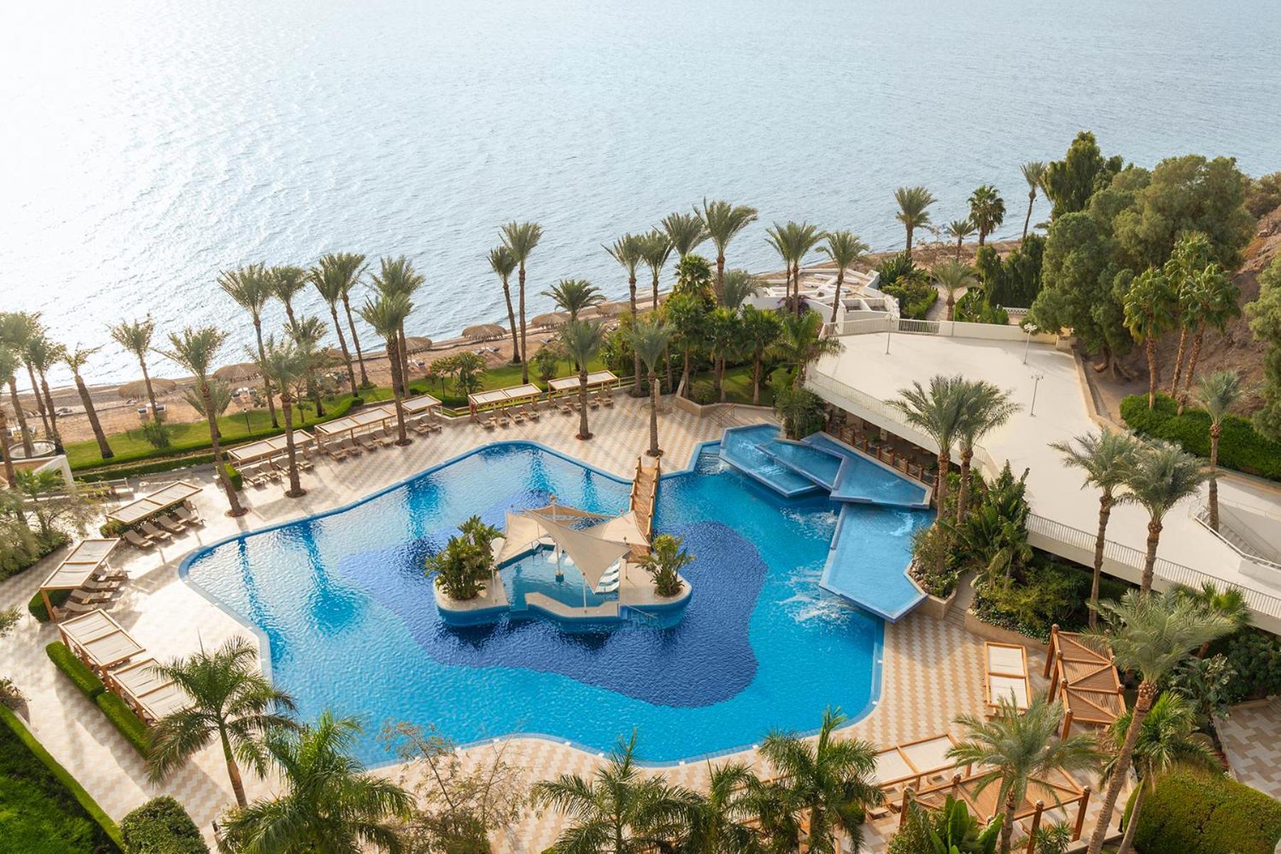 Steigenberger Hotel & Nelson Village, Taba Exterior foto The photo depicts a luxurious resort area featuring a large, beautifully designed swimming pool. The pool has a unique shape, with sections for lounging and relaxation, surrounded by palm trees and greenery. In the background, you can see the ocean, 
