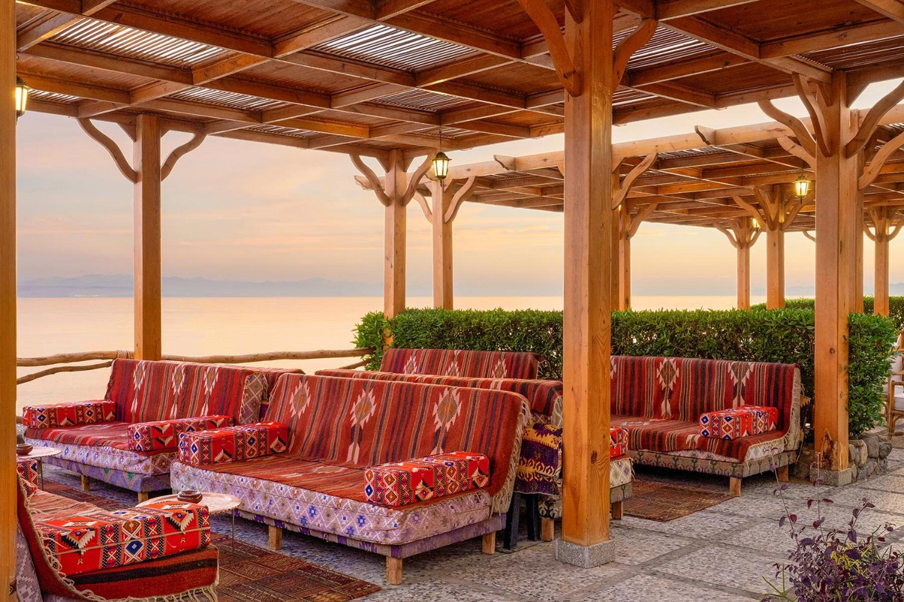 Steigenberger Hotel & Nelson Village, Taba Exterior foto The image shows a beautifully designed outdoor seating area with a wooden pergola structure. The seating consists of comfortable couches adorned with vibrant, patterned cushions, offering a cozy and inviting atmosphere. The space is illuminated by wa